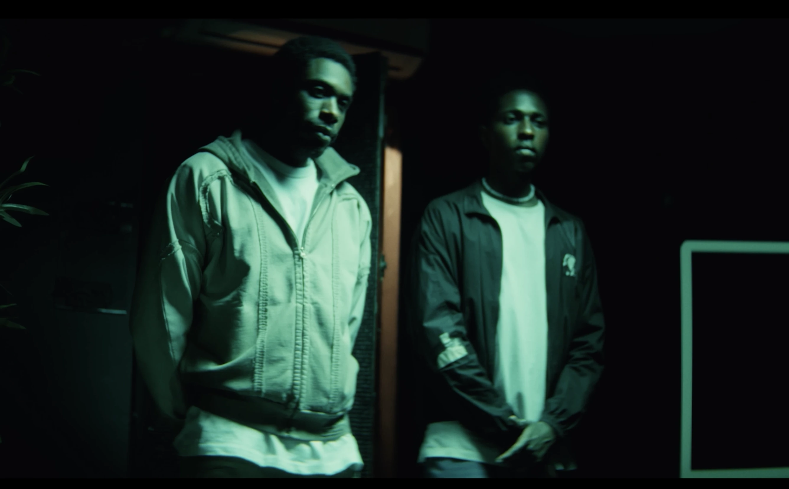 Two men stand side by side in a dark, green-lit room.
